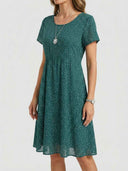 Green mini dress with white polka dots, short sleeves, and gathered waist, angled view.