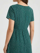 Green mini dress with white polka dots, elastic waist, and short sleeves, back view.