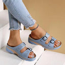 Light blue platform wedge sandals with two adjustable buckle straps and perforated floral detailing on upper, angled front view worn with jeans.