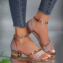 Rose gold glitter block heel sandals with metallic ankle strap, buckle closure, crystal charm pendant, and studded geometric heel — front angled view.