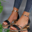 Black open-toe block heel sandals with gold metallic trim, ankle strap and buckle closure — angled front view on neutral background.