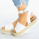 White espadrille flatform sandal with wide open-toe band, ankle buckle strap and woven jute platform sole, angled front view on foot.
