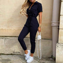 Navy belted bodycon jumpsuit with decorative buttons, front view on stone background.