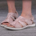 Blush pink closed toe cushioned walking sandals with woven lattice upper, secure heel strap and flat white rubber sole, worn on feet — front angled view.