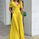 Yellow jumpsuit with V-neck, puff sleeves, and wide legs, holding a green clutch, front view.