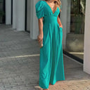Teal jumpsuit with puffed sleeves, V-neck, and wide legs, angled outdoor view.