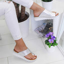 White open-toe wedge mule sandals with metallic copper-tone trim on toe-band and chunky dark sole, styled on white tile floor.