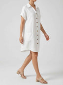 White textured mini shirt dress with brown buttons, two pockets, and short sleeves, angled view.