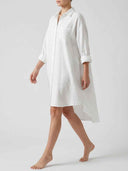 White mini sundress with rolled sleeves, chest pocket, and high-low hem, angled side view.
