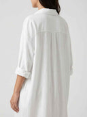 White mini sundress with collar, rolled sleeves, and back pleats, angled back view.