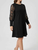 Black mini dress with sheer, sequined floral long sleeves, angled front view.