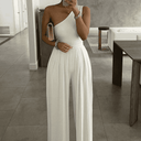 White asymmetrical one-shoulder jumpsuit with wide pleated legs, front view in a modern room.