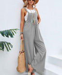 Gray flared jumpsuit with button straps and front pockets, angled view on white background.