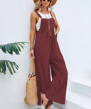 Maroon flared jumpsuit with white tank top, straw hat, and bag, angled front view.