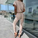 Beige short-sleeve jumpsuit with elastic waist, shown from the back on a patio.