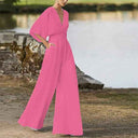 Pink dolman sleeve knit jumpsuit with V-neckline, front view outdoors by water.