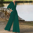 Dark green dolman sleeve knit jumpsuit with V-neck, angled front view by water.