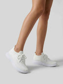 White knit supportive trainers on a model's feet showing lace-up fastening and cushioned sole, angled view.