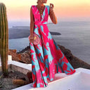 Pink and blue floral maxi dress with deep V-neck, worn outdoors with ocean background, front view.