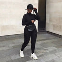 Black slim-fit jumpsuit with mock neck, worn with a black fanny pack and white sneakers, full body.