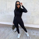 Black slim-fit jumpsuit with long sleeves, worn by a model with sunglasses, angled view.