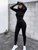 Black slim-fit jumpsuit with long sleeves, worn by a model with a cap, full-body view.