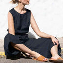 Navy cotton-linen jumpsuit with relaxed crew neckline, worn by a model sitting on the ground.