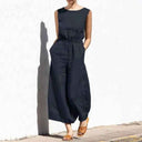 Navy cotton-linen jumpsuit with relaxed crew neck, front view on white wall background.