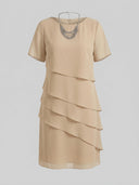 Tan mini dress with short sleeves, tiered ruffles, and a silver necklace, front view on gray background.