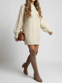 Cream cable knit mini dress with long sleeves, worn with brown boots and purse, angled view.