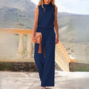 Navy blue sleeveless wide-leg jumpsuit, front view on a balcony with mountains.