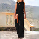 Black sleeveless jumpsuit with high neck and wide legs, holding peach clutch, full front view.