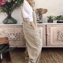 Tan jumpsuit with pockets over a white shirt, side view, in front of a decorative cabinet.