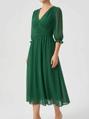 Green V-neck mini dress with ruched waist and sheer long sleeves, angled front view on white background.