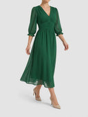 Green V-neck mini dress with sheer long sleeves and ruched waist, angled front view.