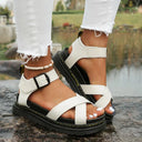 White chunky platform sandals with crossover toe straps and buckle ankle strap, worn with white distressed jeans, angled front view.