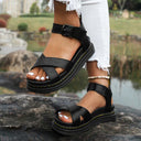 Black chunky platform sandals with crossover toe straps and buckle ankle strap, angled side view worn with white jeans.
