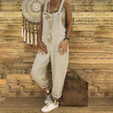 Light beige linen overalls with long beaded necklace, front view on wood background.