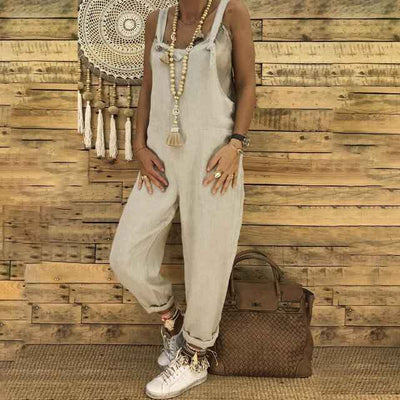 Light beige linen overalls with long beaded necklace, front view on wood background.