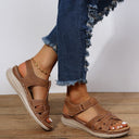 Brown flatform sandals with adjustable hook-and-loop ankle strap and cushioned footbed, angled side view on wooden surface.