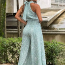 Light green jumpsuit with white abstract print, halter neck tie, back view.