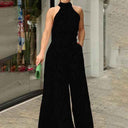 Black halter neck jumpsuit with subtle print, front view, urban background.
