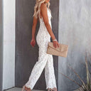 White lace jumpsuit with thin straps, side view, holding a beige clutch.