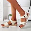 Beige low wedge sandals with crossover strap and cushioned platform sole, worn on feet, angled side view.