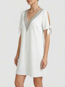White V-neck dress with silver trim, tie sleeves, and gold necklace, angled front view.