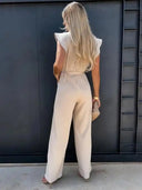 Beige ruffled sleeve jumpsuit with coordinating waist belt, back view against dark wall.
