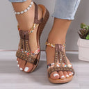 Brown embellished flatform sandals with gold rhinestone cage straps and floral-print fabric detail, open-toe T-bar style on model, angled front view.
