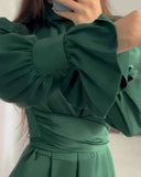 Dark green dress with ruffled sleeves, pleated skirt, and waist detail, angled view.