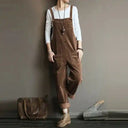 Brown corduroy sleeveless jumpsuit with side pockets, worn over a white long-sleeve shirt, full view.
