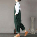 Dark green corduroy sleeveless jumpsuit with side pockets, worn over a white shirt, side view.